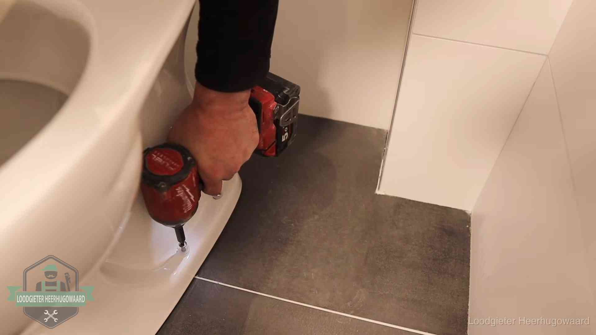 Loodgieter zet de voet van een wc-pot vast op de tegelvloer in Heerhugowaard